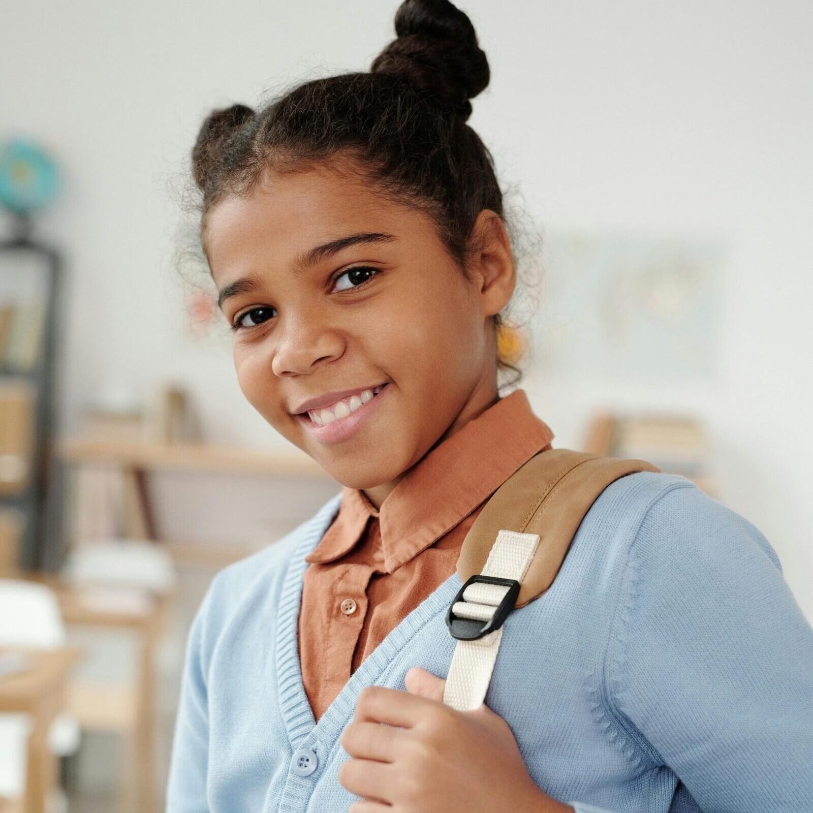 Happy girl with backpack in classroom, ready for school day.