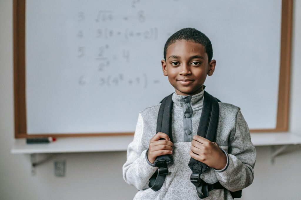Smiling boy with backpack in classroom, ready for math class.